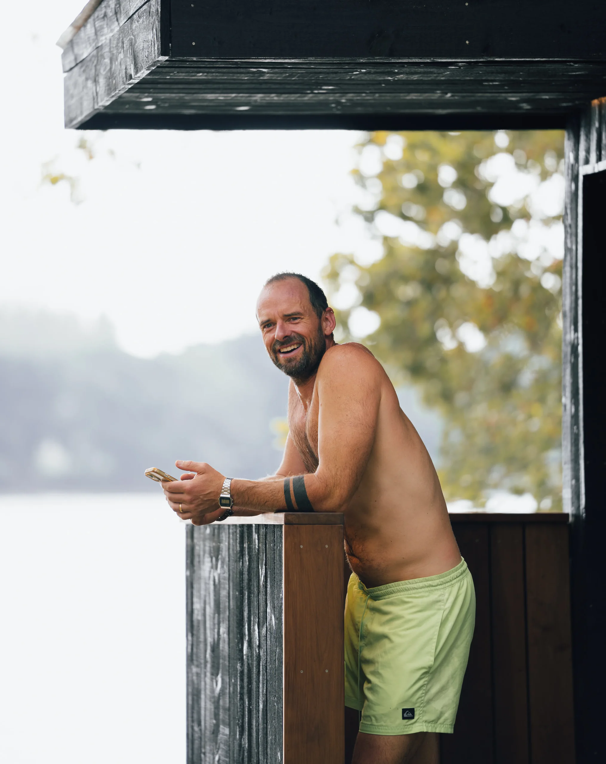 A smiling member leaning on the Bosham Sauna porch rail between rounds.